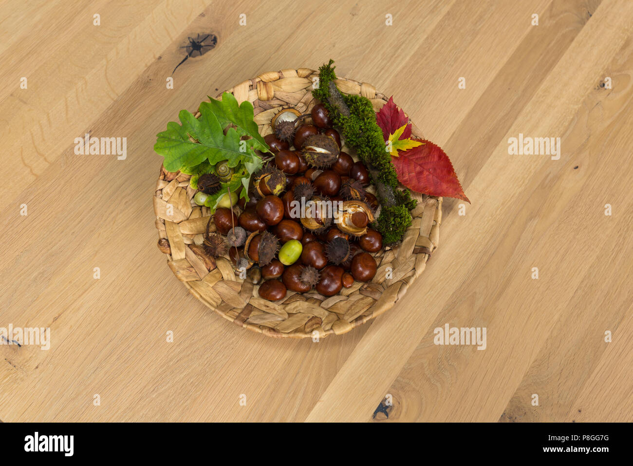 Decorazione d'autunno - castagne, foglie e ghiande su una piastra intrecciato su uno sfondo di legno n. 2 Foto Stock