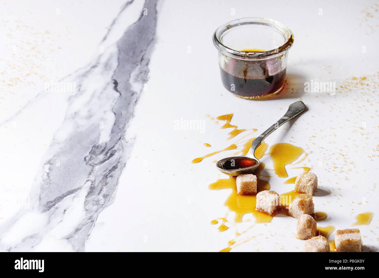 In casa liquido trasparente marrone zucchero caramellato in un barattolo di vetro con il cucchiaio e la canna da zucchero Zollette di zucchero bianco su sfondo marmo. Copia dello spazio. Foto Stock