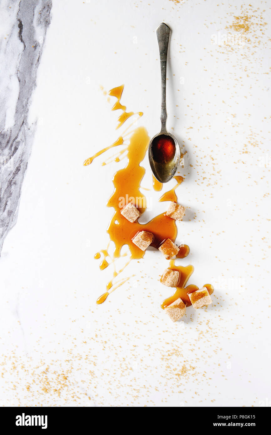 In casa liquido trasparente marrone zucchero caramellato in cucchiaio vintage e della canna da zucchero Zollette di zucchero bianco su sfondo marmo. Appartamento laico, spazio. Foto Stock