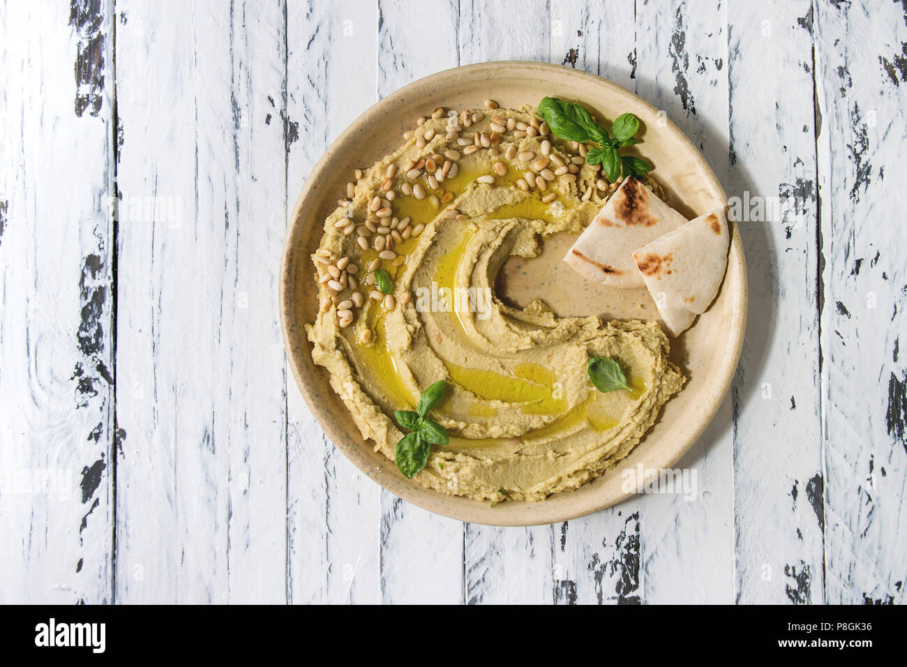 In casa tradizionale diffusione hummus con pinoli, olio di oliva, basilico servito su piastra in ceramica con pane pita su bianco tavolato in legno sfondo. L piatto Foto Stock