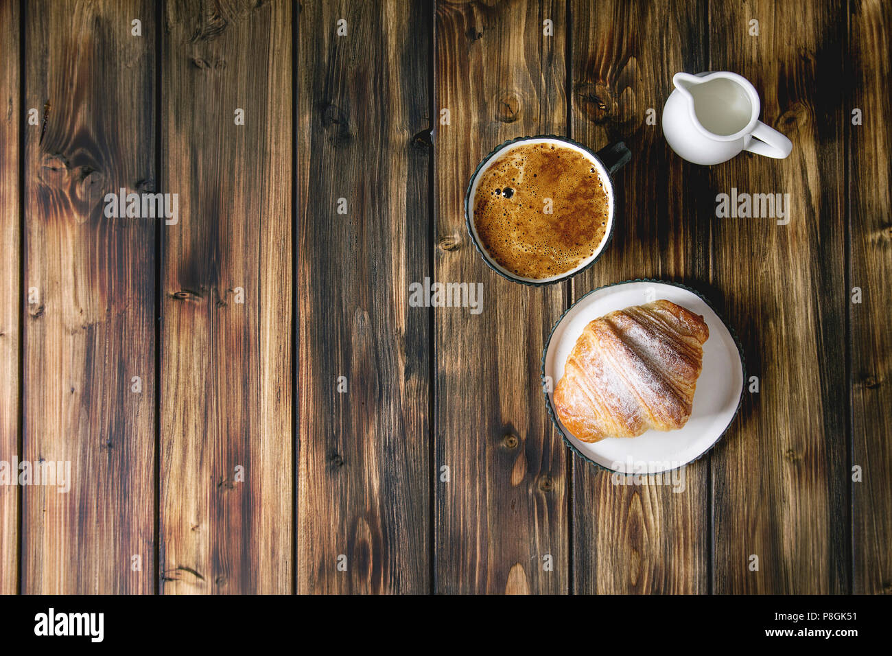 Croissant fatti in casa con lo zucchero in polvere, tazza di caffè, brocca del latte su tavola in legno sfondo. Appartamento laico, spazio. Foto Stock