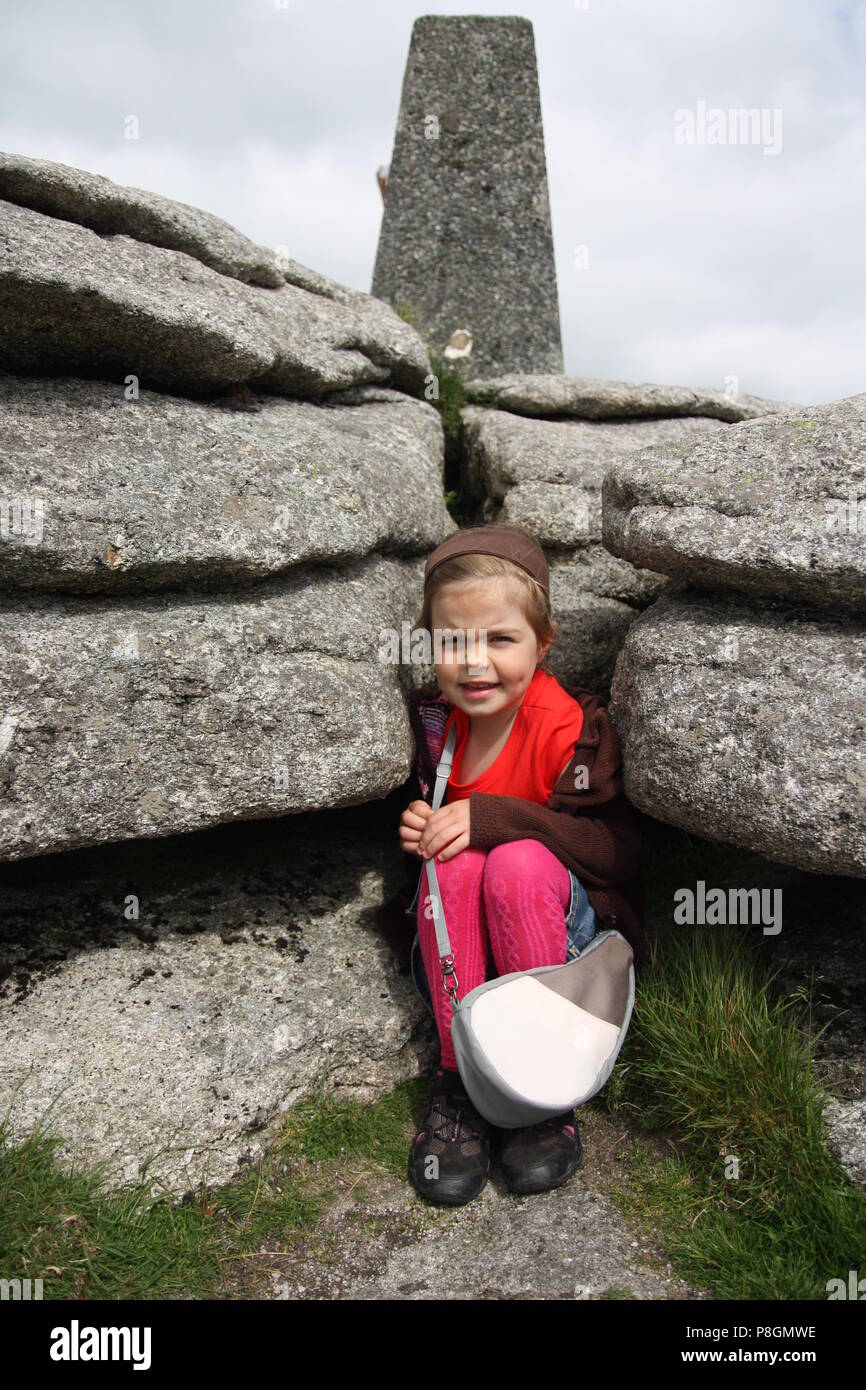 Ragazza giovane con la borsetta sul paese ramble a dartmoor tor accovacciato tra le rocce Foto Stock