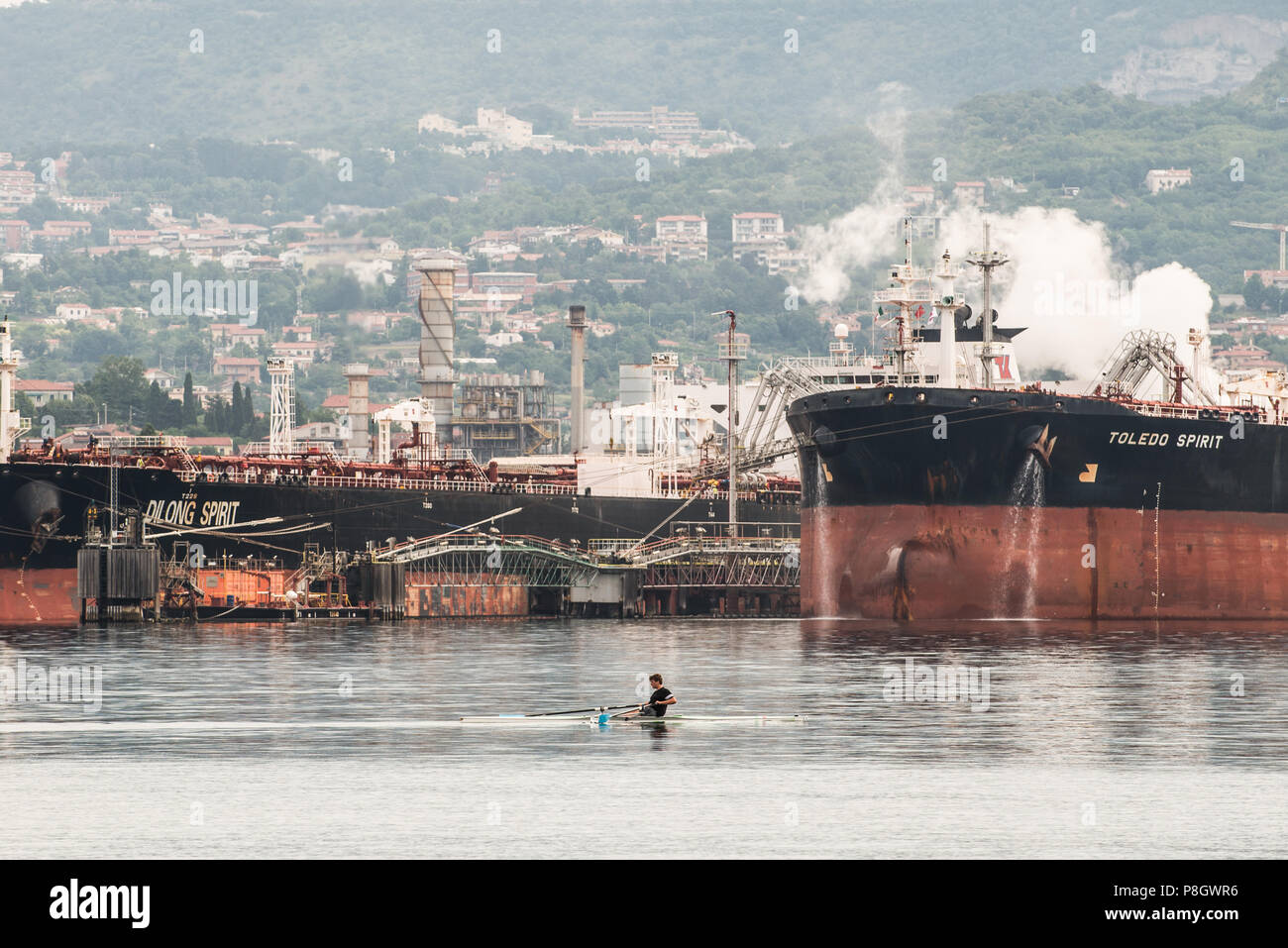 Un canoeist tarining davanti Dilong lo spirito e lo spirito di Toledo petroliere ormeggiate nel porto di Trieste, Italia Foto Stock