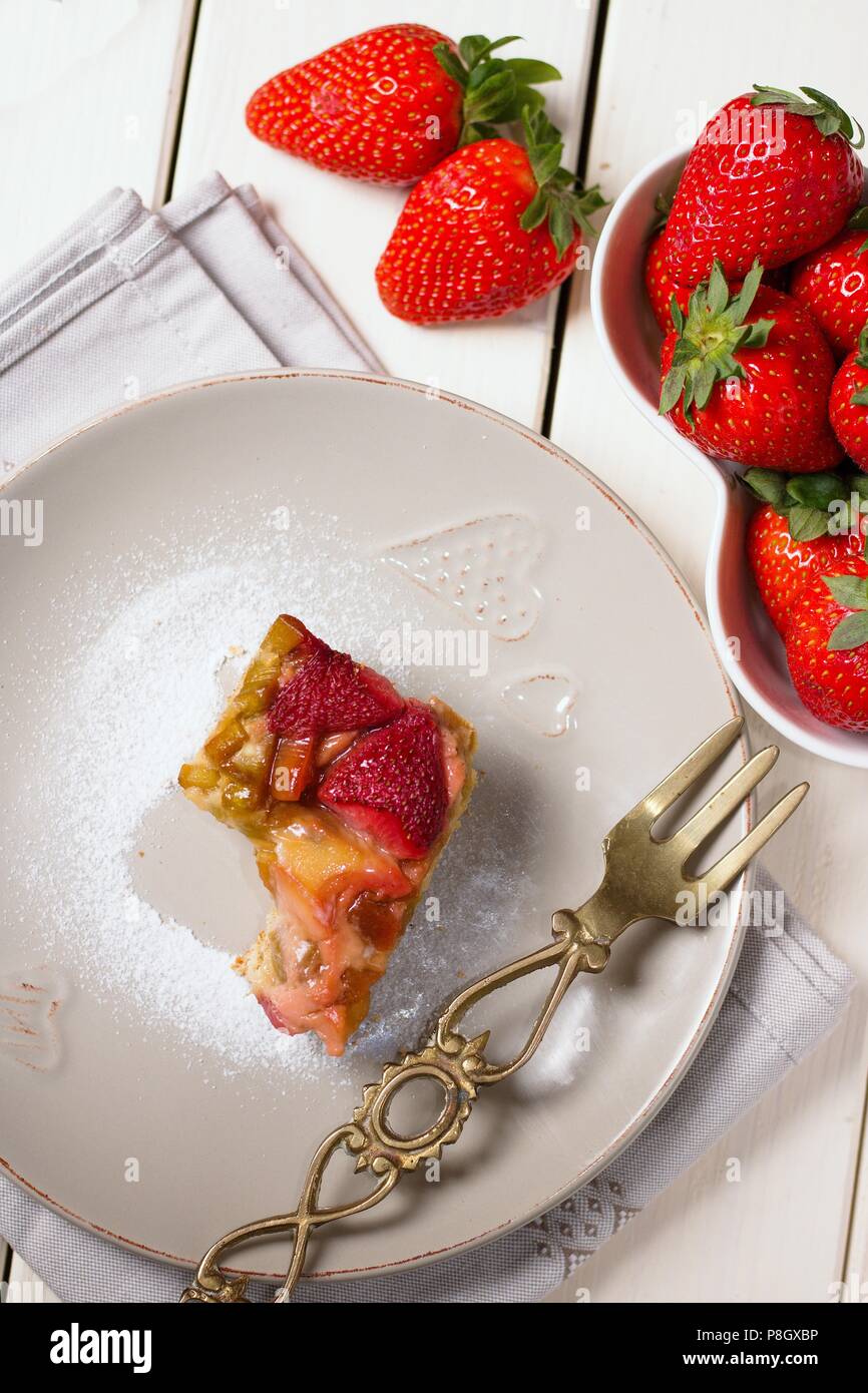 Direttamente sopra vista sulla metà mangiato pezzo di fragole e rabarbaro torta sulla tavola di legno tavolo e forcella in ottone Foto Stock