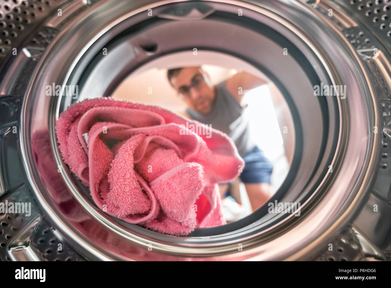 Giovane uomo che fa servizio lavanderia vista dall'interno della macchina di lavaggio Foto Stock