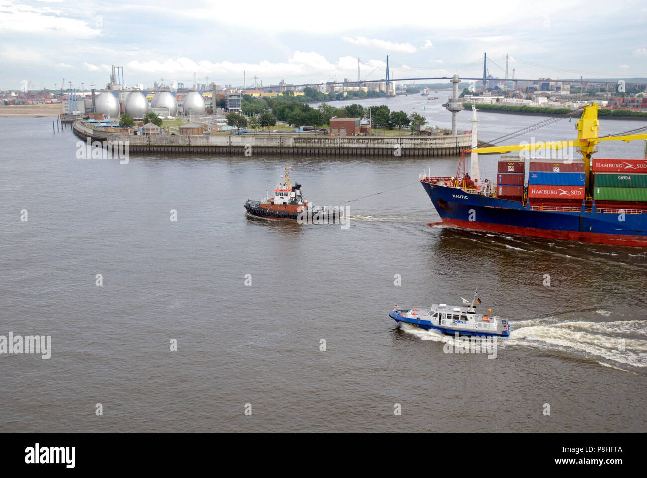 Schlepper manoevrieren auf der Elbe einen Container-Frachter in den Hamburger Hafen. Im Hintergrund die Koehlbrandbruecke. Foto Stock