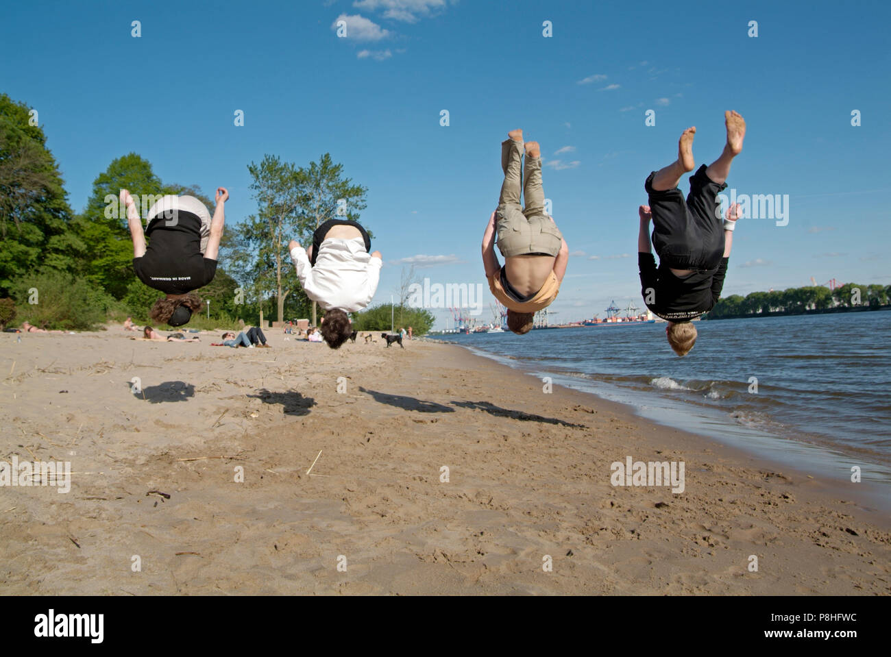 Vier junge Maenner trainieren gemeinsam ihren Rueckwarts-Salto am Hamburger Elbe-Strand in Oevelgoenne. Foto Stock