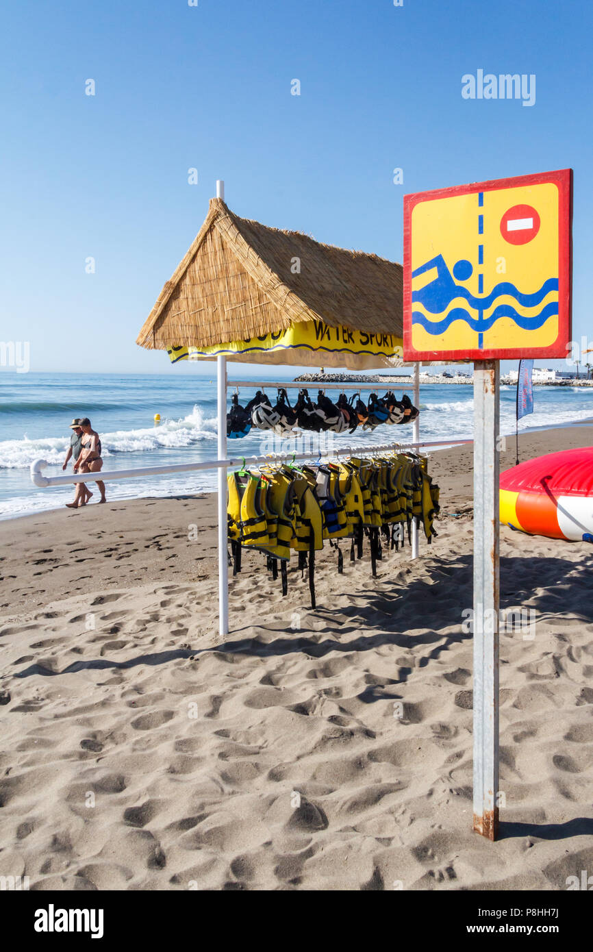Benalmadena - 19/6/2018: un giovane a piedi lungo la spiaggia oltre a sport acquatici area designata. Vi sono anche aree designate nuoto. Foto Stock