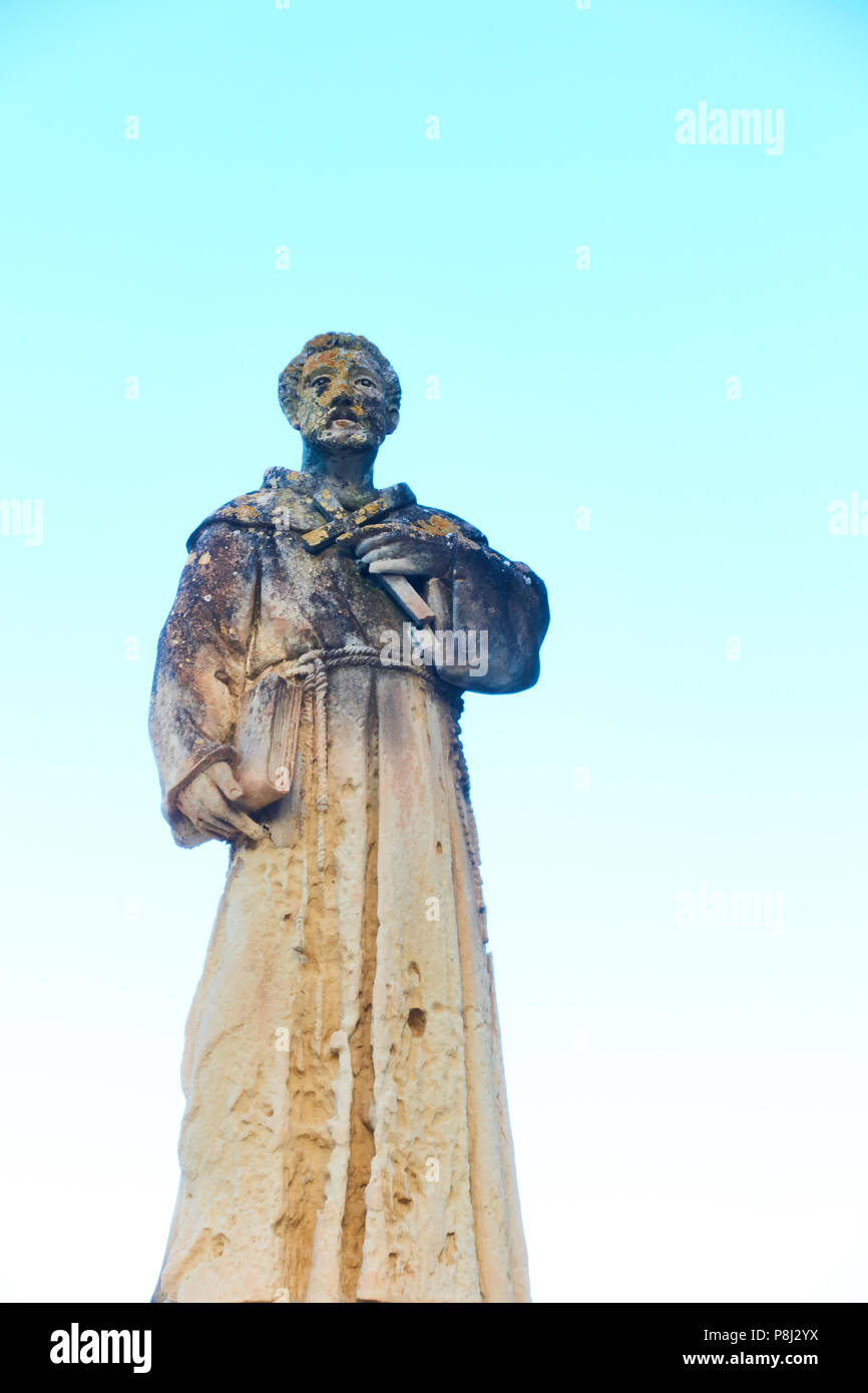 Uno sbriciolamento statua del pellegrino o saint nell'Addolorata cimitero, Malta, con un pastello cielo dietro Foto Stock