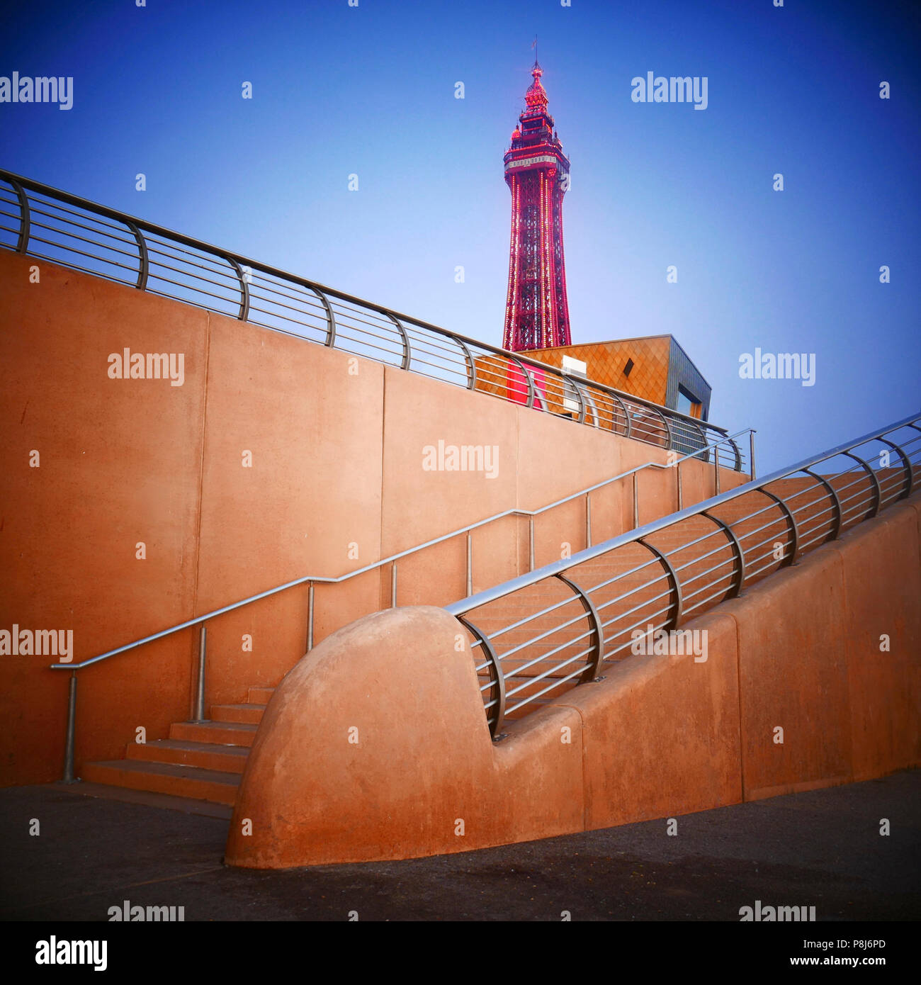 La Blackpool Tower splende al crepuscolo sopra i gradini di cemento che conducono giù dal lungomare Foto Stock