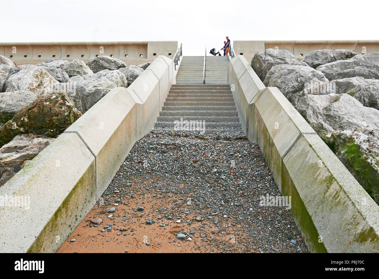 L uomo e la donna con la PRAM camminando lungo il mare Rossall difese parete in corrispondenza di Fleetwood, nel Lancashire,aperto 2018 Foto Stock