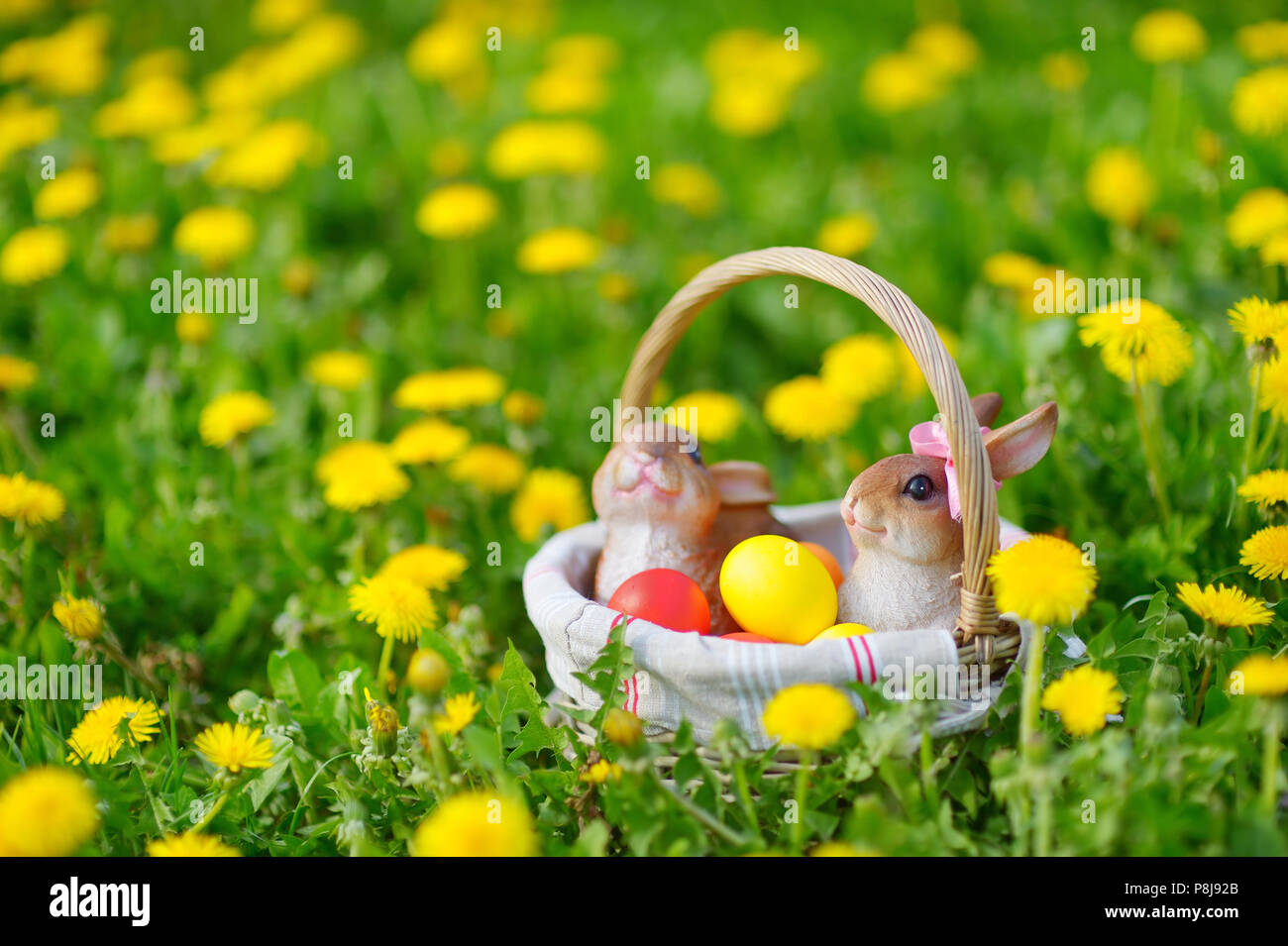 Colorate le uova di pasqua in un cesto su un prato con due coniglietti Foto Stock