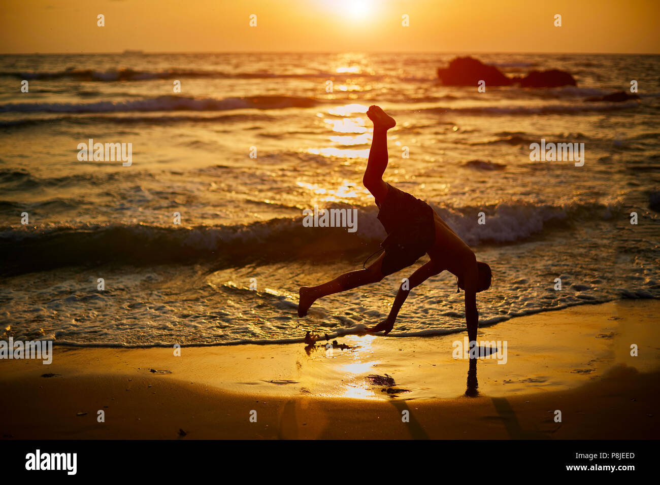 Giovane ragazzo giocare capoeira in spiaggia. Il bambino è felice e  divertirsi a fare dello sport vicino al mare durante il tramonto. Miglior  Vacanze estive capovolto. Silhouette di un ragazzo che acrobatici