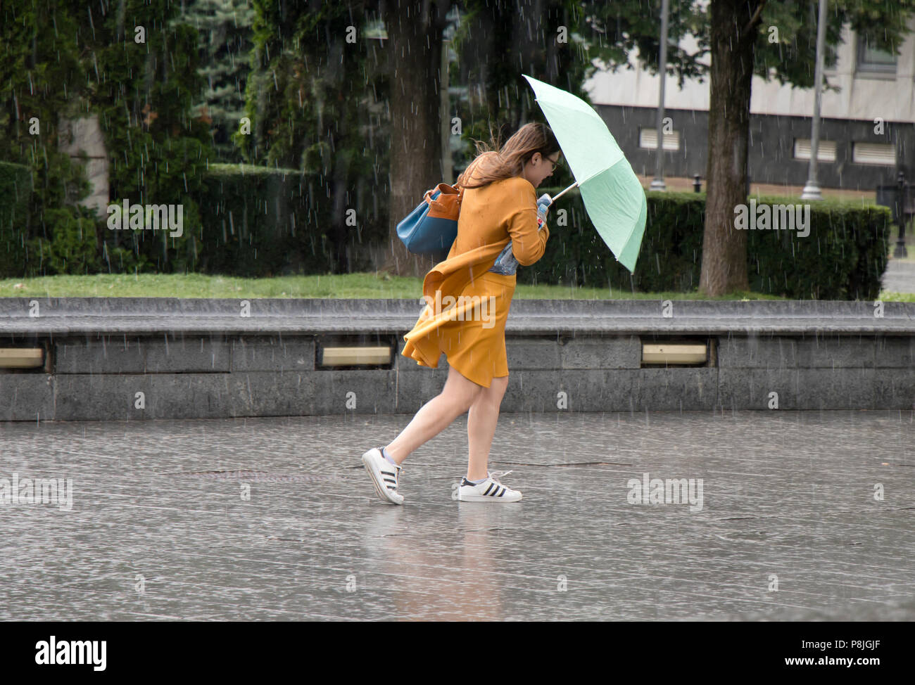 A Belgrado, in Serbia - Giugno 14, 2018: una giovane donna che gira sotto ombrellone in improvviso molla pesante ventoso pioggia nel parco della città , tenendo una bottiglia di Foto Stock