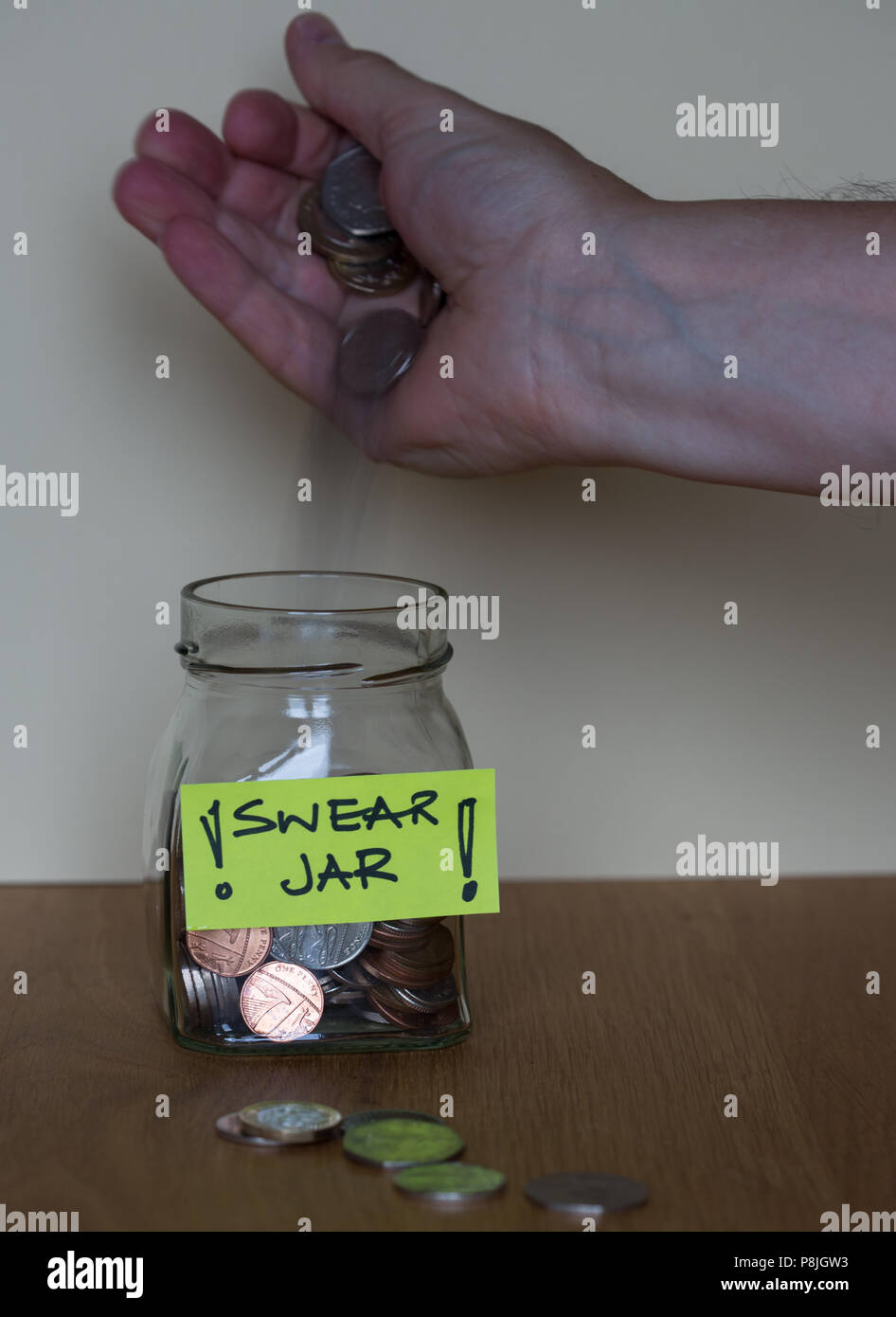 Un vetro giurare jar con un'etichetta gialla su un tavolo di legno con una mano mettere il denaro nel vaso Foto Stock