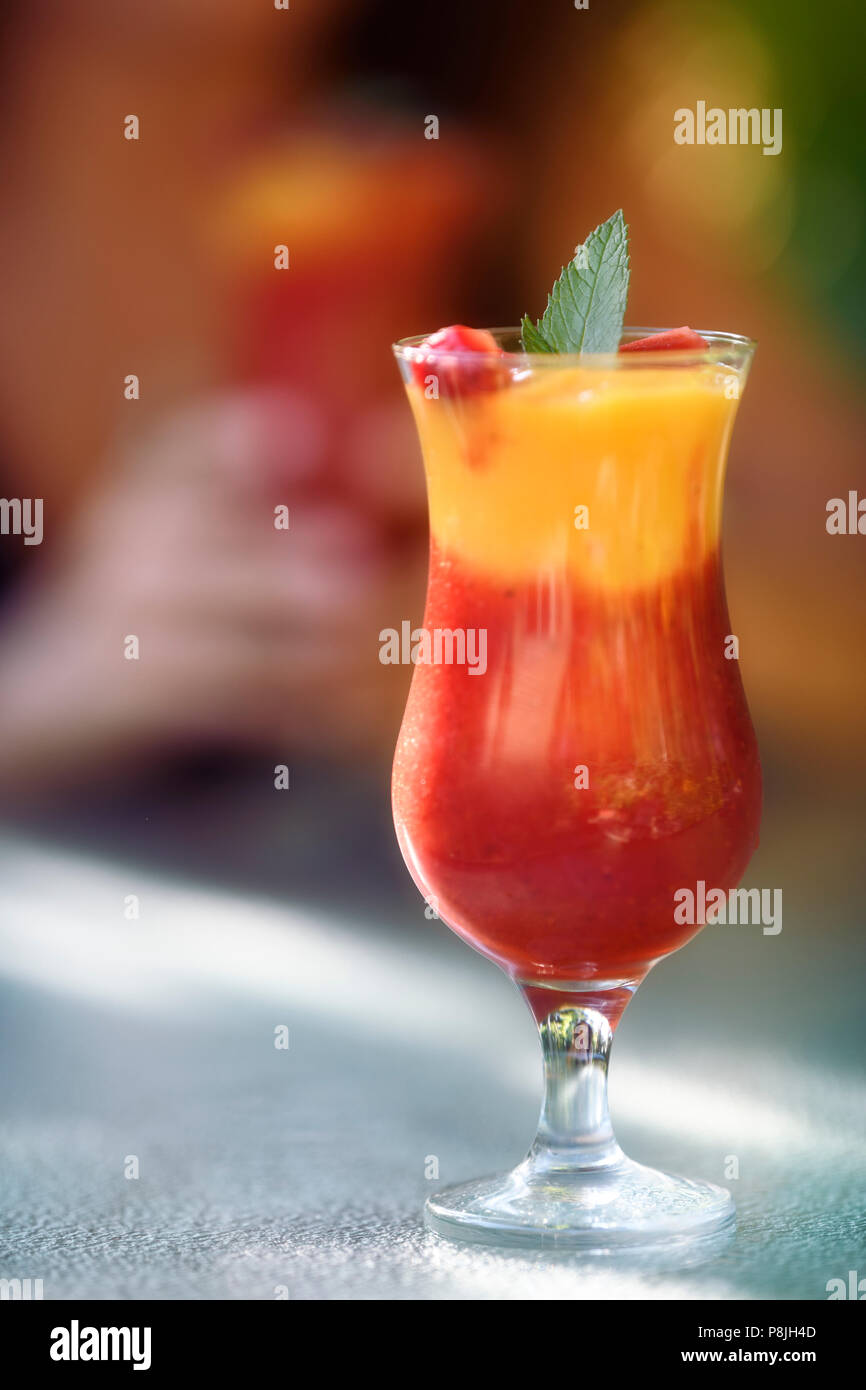 Vergine Strawberry Mango Margarita mocktail. Colorati cocktail analcolico, frullato di frutta bere su una tabella con una donna tenendo premuto un altro vetro in Foto Stock