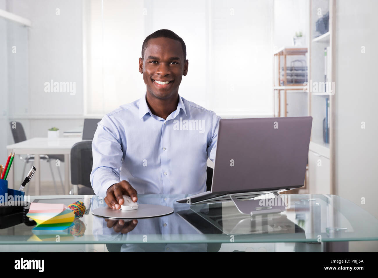 Ritratto di giovane imprenditore sorridente utilizzando laptop al lavoro Foto Stock