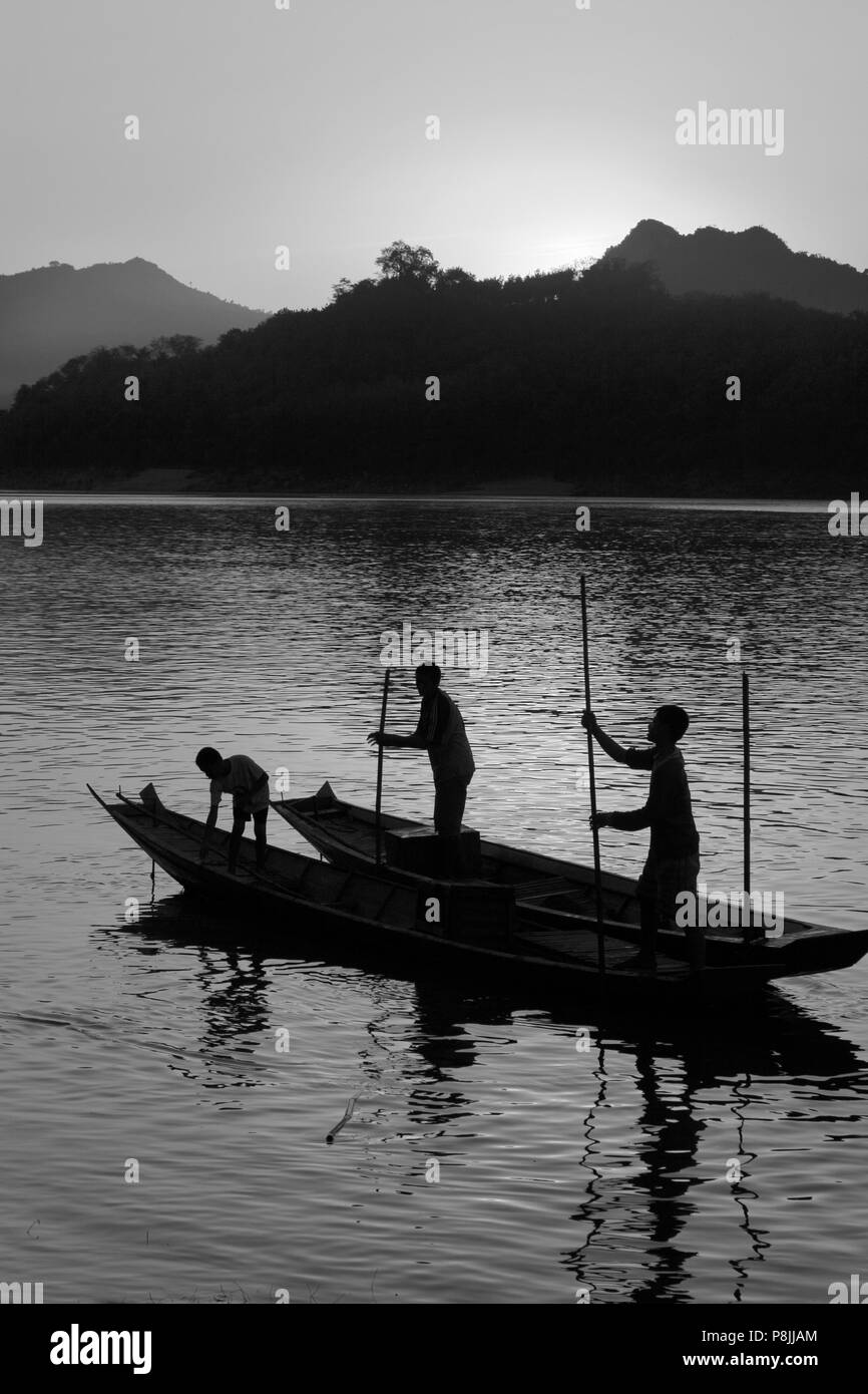 Il sole tramonta su una collina sul fiume Mekong scontornamento laotiani il polling della loro barca fluviale che corre attraverso - Luang Probang, LAOS Foto Stock
