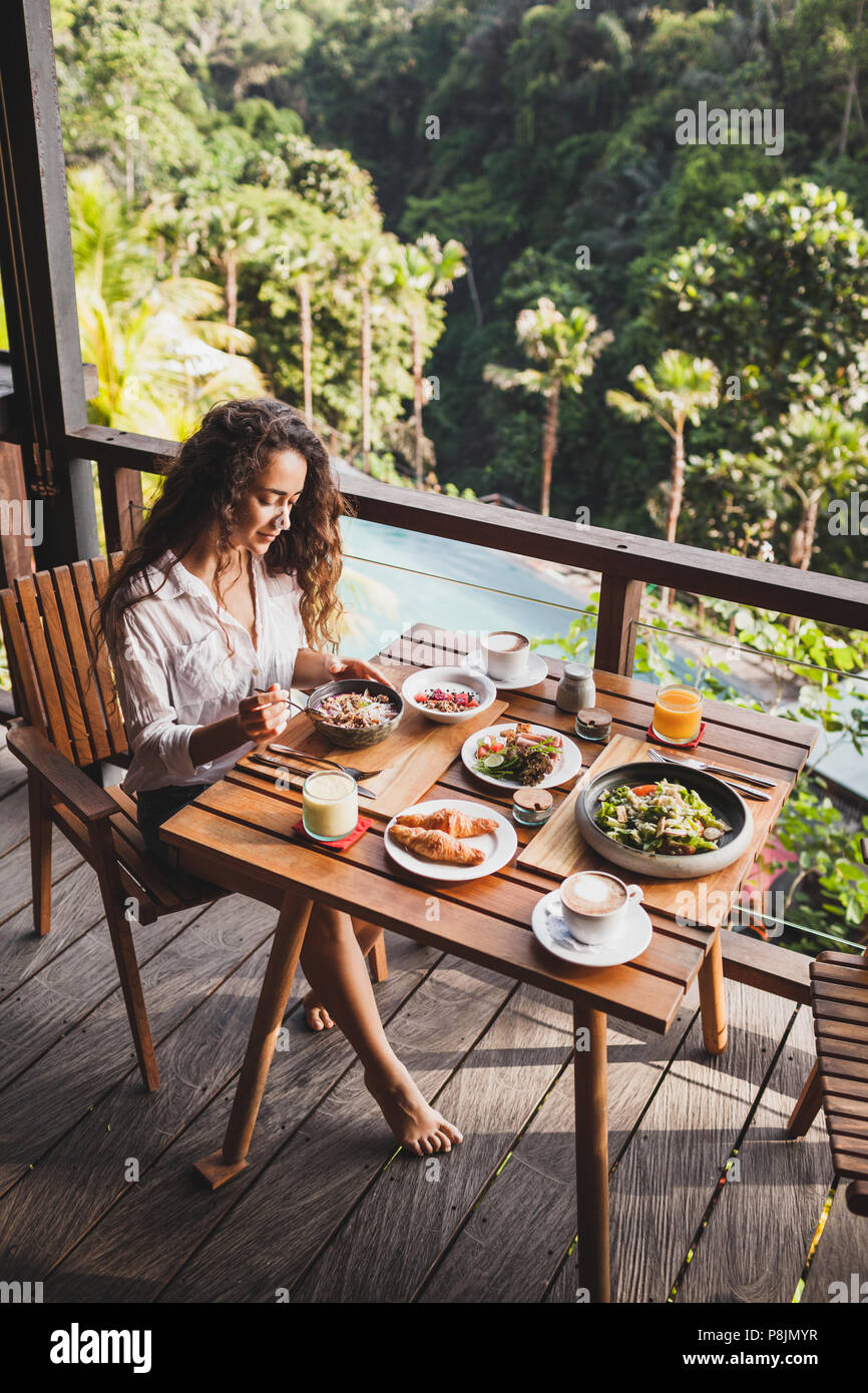Donna gustando la prima colazione sulla terrazza con straordinaria vista Giungla Una camicia bianca e jeans corti Foto Stock