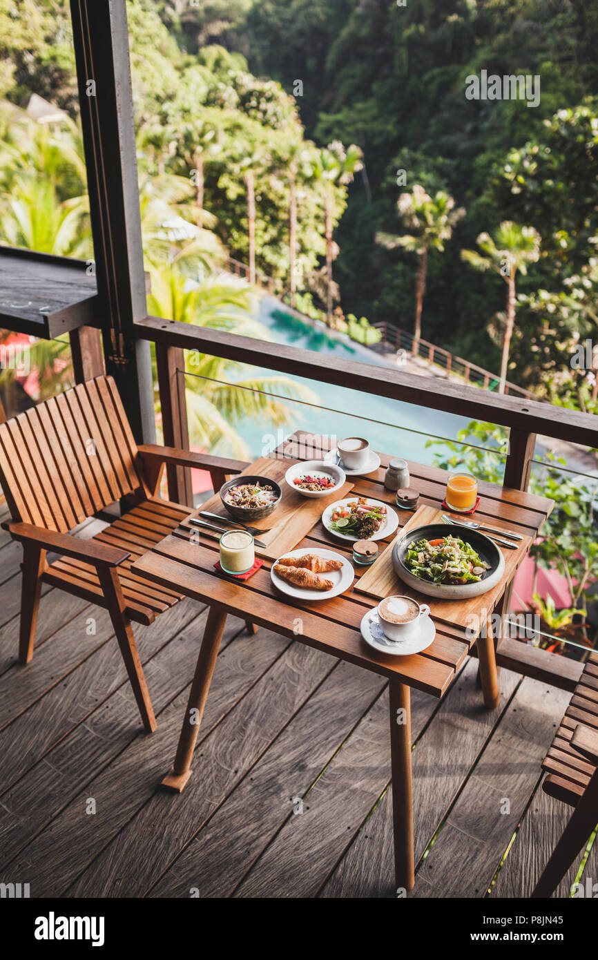 Tabella con la prima colazione servita sulla terrazza in legno con piscina e vista Giungla di Bali Foto Stock