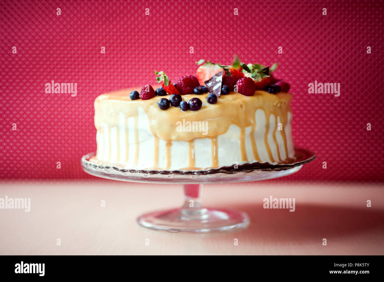 Una torta di compleanno su un piedistallo di vetro sul tavolo, frutta sulla parte superiore. Foto Stock