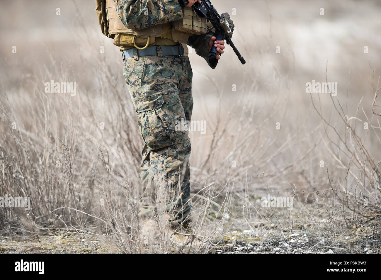 Fucile automatico dettaglio e di mimetizzazione militare uniforme su di un soldato in un campo Foto Stock