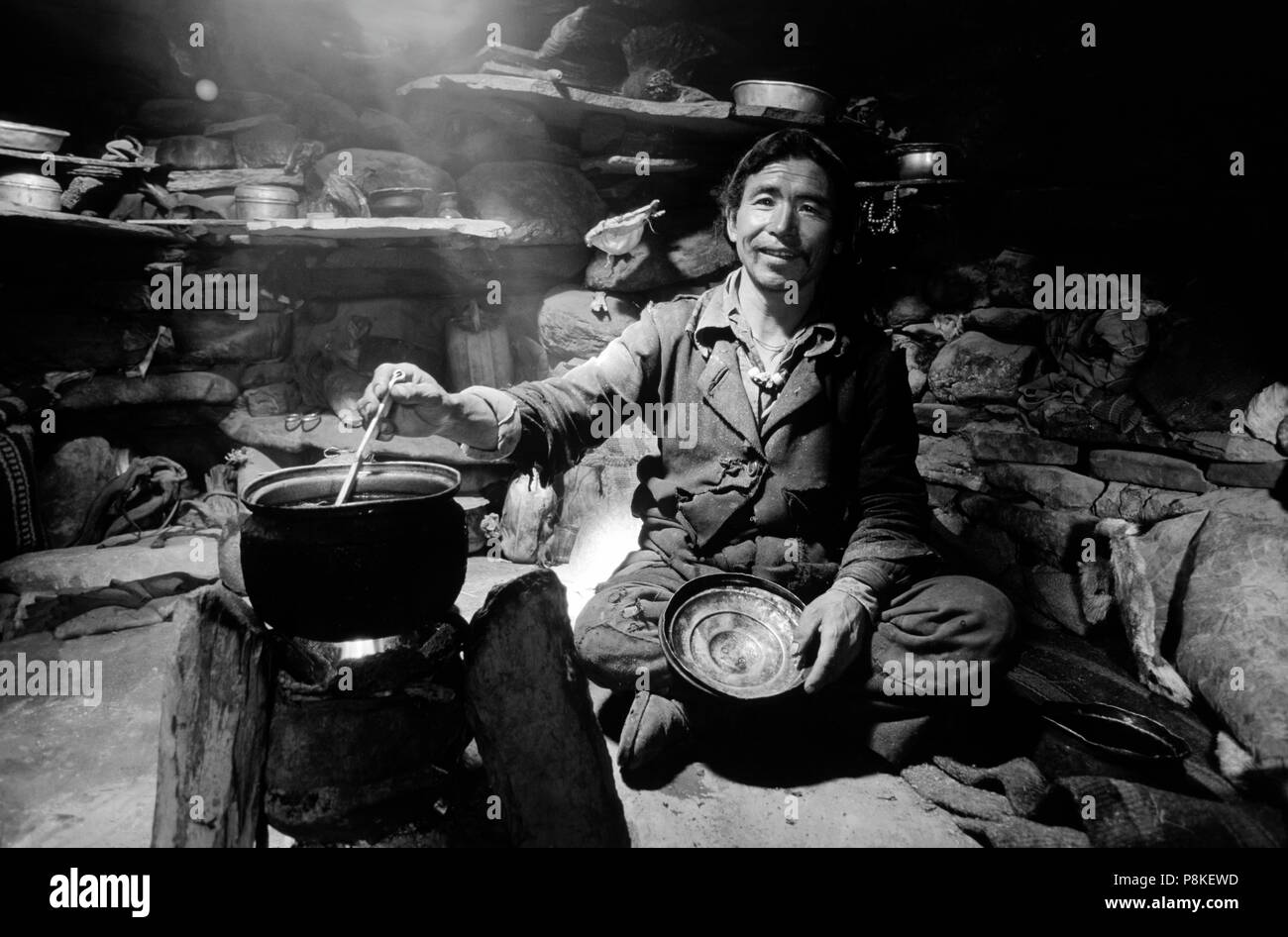 Un uomo DOLPO la cottura di alimenti con utensili da cucina in un yak herder hut - Distretto di DOLPO, NEPAL Foto Stock