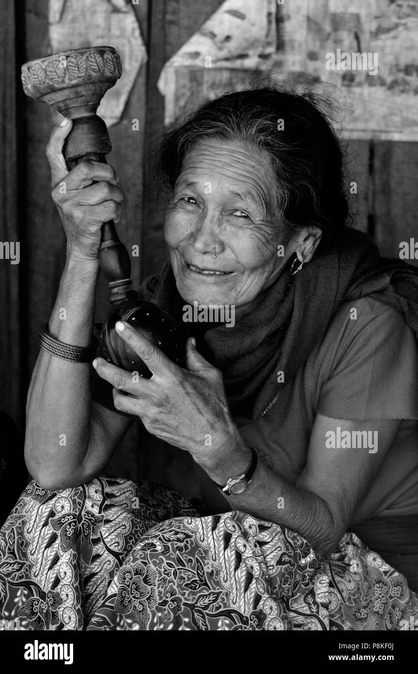 Un villaggio nepalese donna fuma il tabacco in un narghilè PIPE - intorno il MANASLU TREK, NEPAL Foto Stock