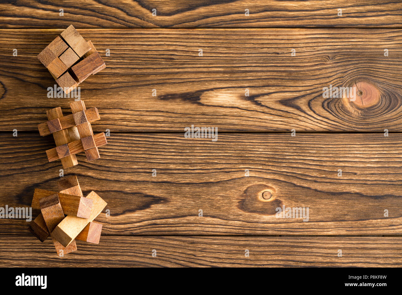 Tre complessi puzzle in legno o brainteasers disposti in una fila come un bordo laterale su un sfondo boscoso con grana di legno decorativo Foto Stock