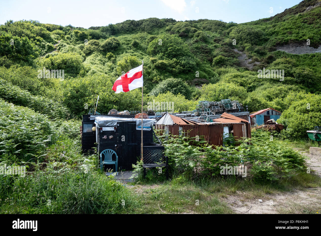 Il treacherous strada giù per le cabine e capanne al vecchio porto di Port Mulgrave sul patrimonio dello Yorkshire Costa, Inghilterra,UK, bandiera inglese battenti. Foto Stock