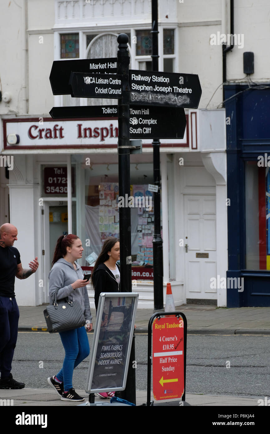 Gli amanti dello shopping a piedi sotto la direzione segno posto nella città del North Yorkshire holiday resort di Scarborough, Regno Unito Foto Stock
