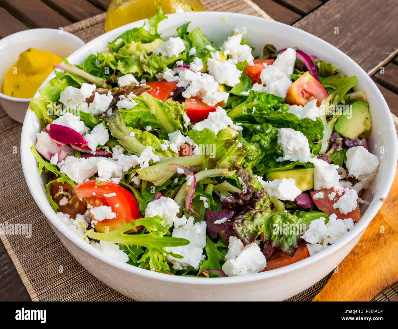 Close up soleggiato insalata estiva in bianco ciotola sul patio esterno tavolo, con lattuga, pomodori, il formaggio feta, cipolla rossa, avocado Foto Stock