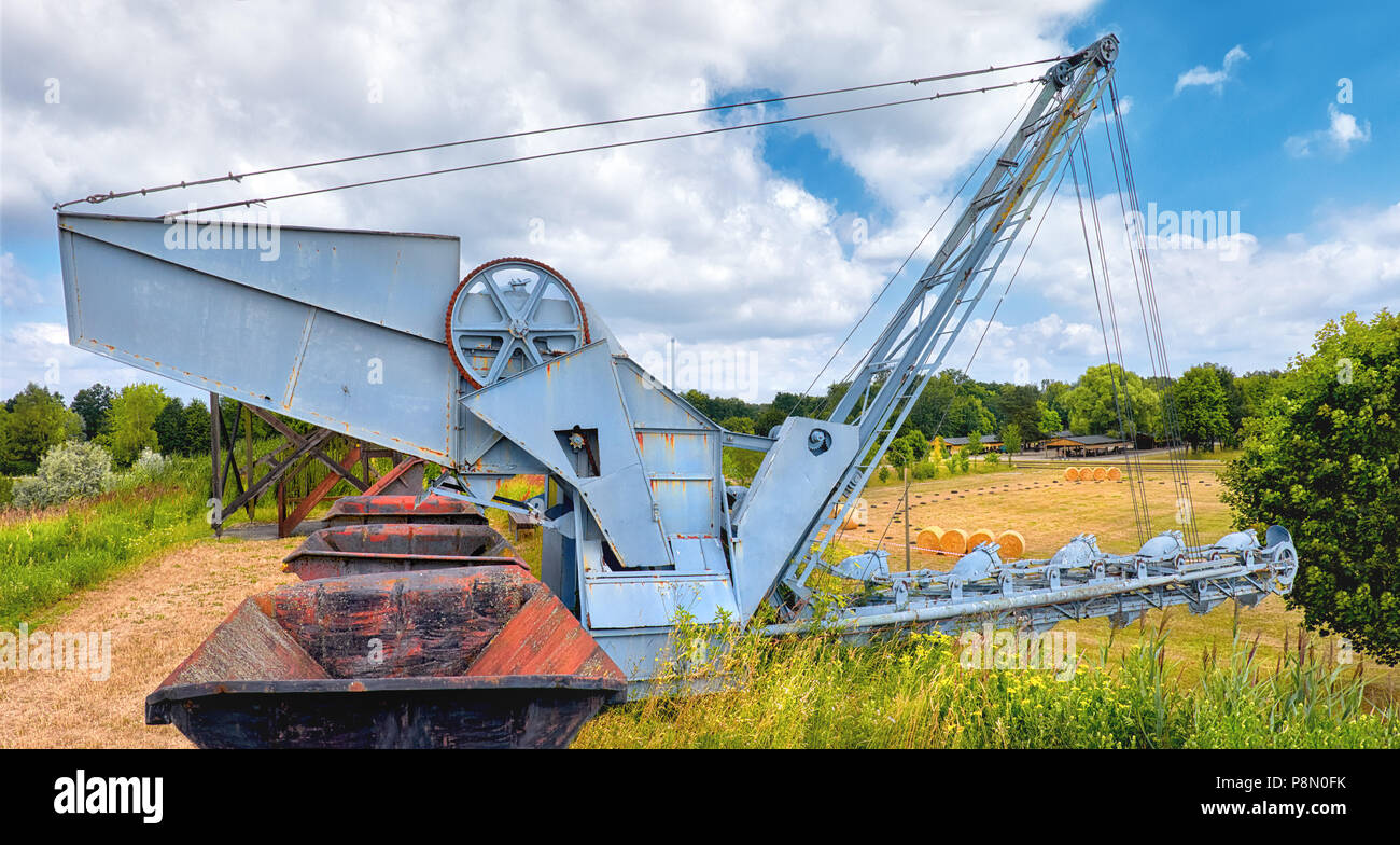 Vecchio benna Escavatore a catena e una fila di carbone vagons su una collina di erba all'esterno. Panoramica di immagini prese nella zona di Brandeburgo, Germania. Foto Stock