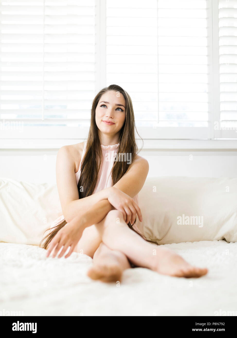 Giovane donna seduta sul letto Foto Stock