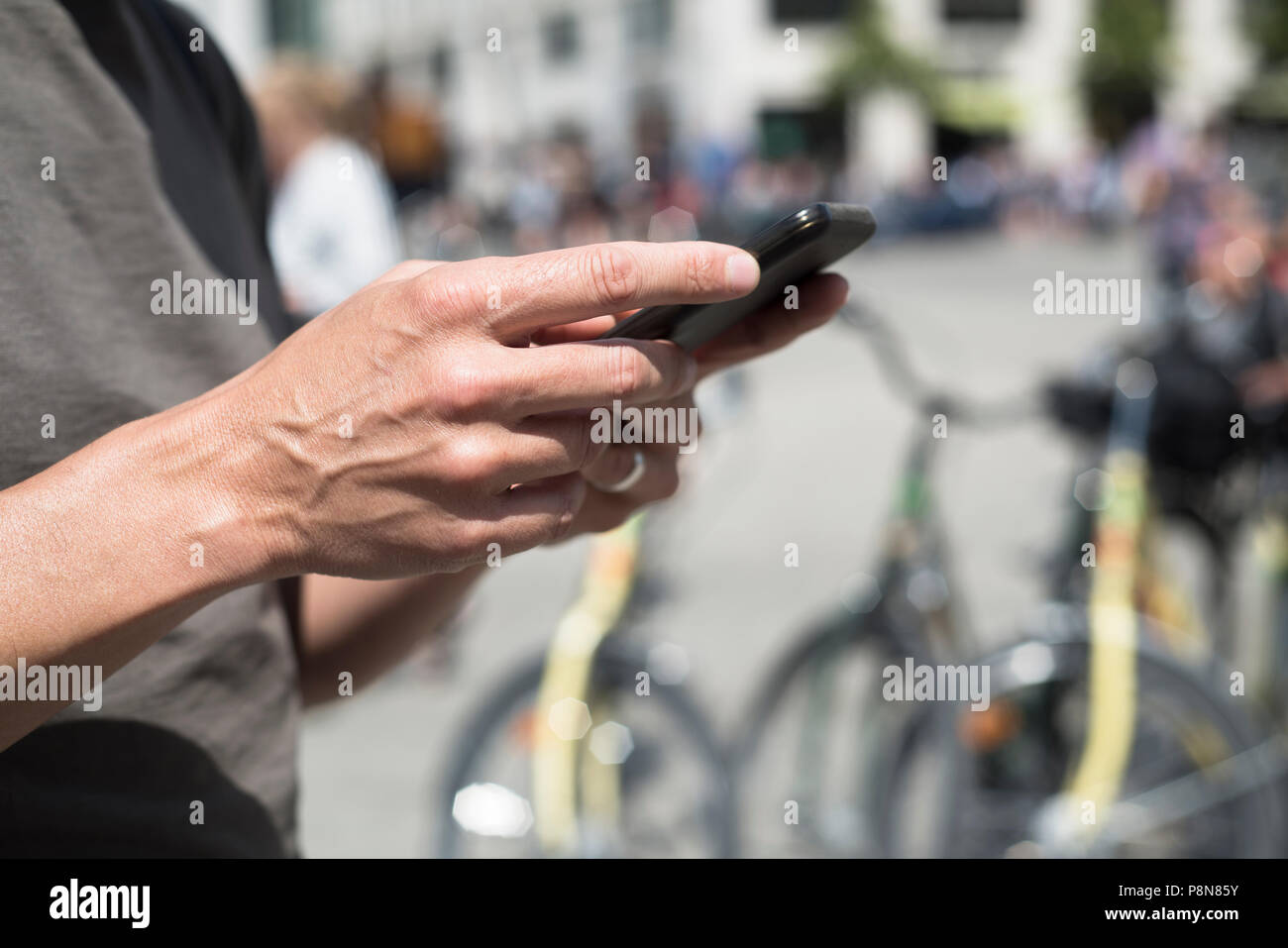 Primo piano di un giovane uomo caucasico utilizzando uno smartphone sulla strada, accanto ad alcune biciclette parcheggiate Foto Stock