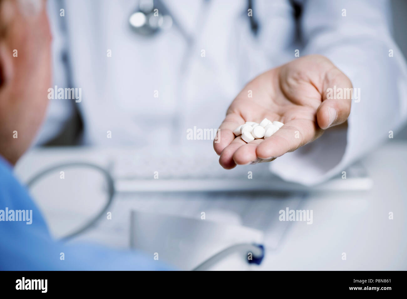 Primo piano di un medico caucasica uomo in camice bianco, dando alcune pillole a un senior caucasica uomo paziente, seduta sia in corrispondenza di un banco medici Foto Stock