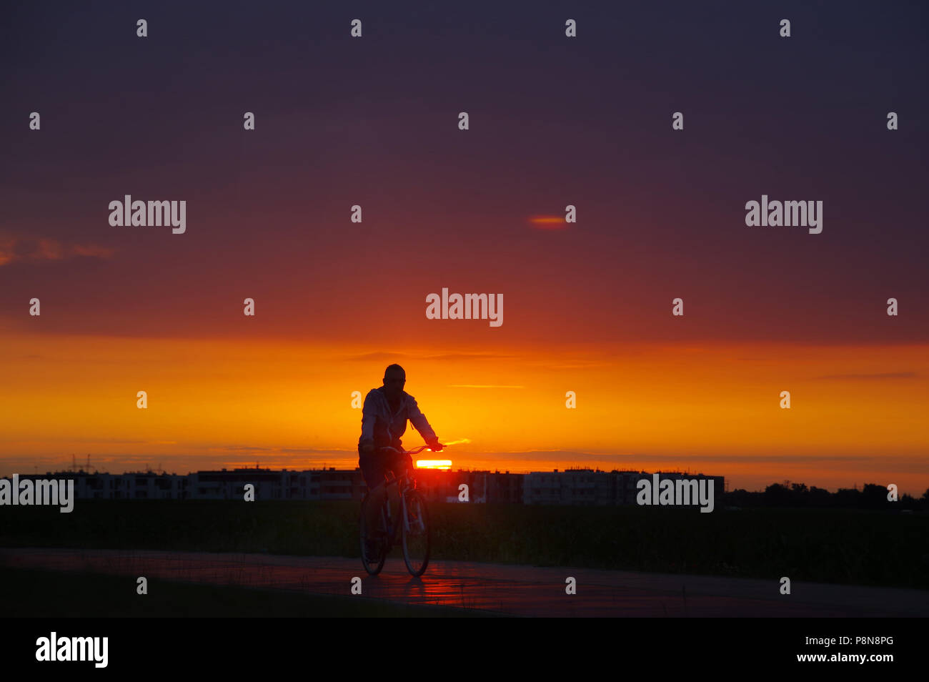 Silhouette di uomo sulla bicicletta con la città e il bel tramonto in background Foto Stock