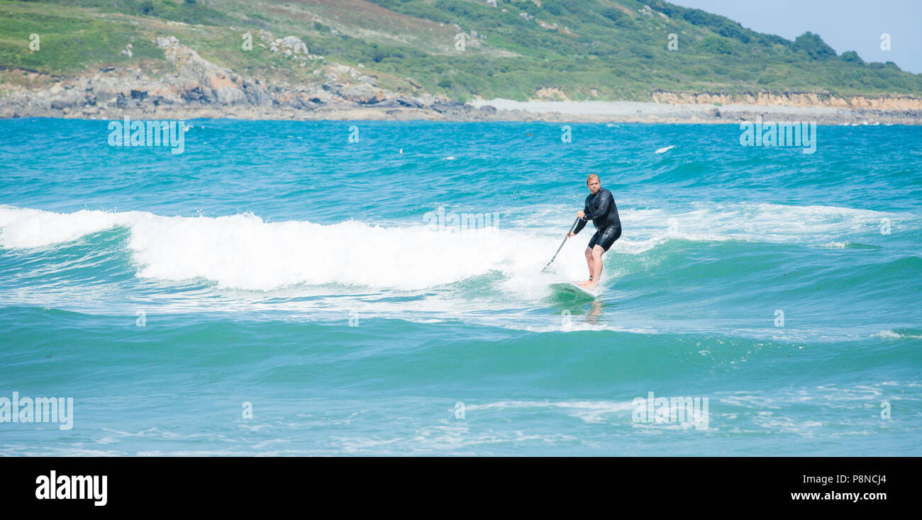 Un surfista in Cornovaglia usando una racchetta board e remo a cavalcare le onde bianco sull'oceano Foto Stock
