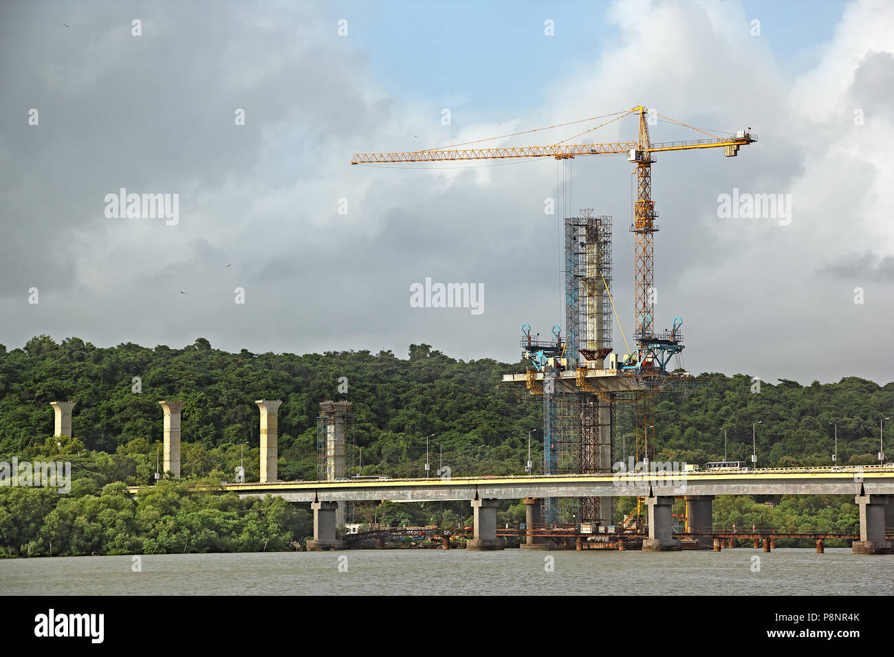 Alte colonne di cemento e il piano viene eretta la torre con gru e altre attrezzature per il terzo ponte sul fiume Mandovi in Goa, India Foto Stock