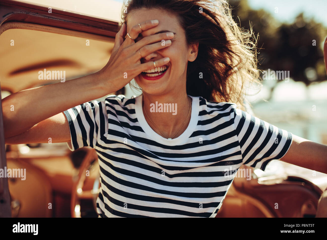 Donna in piedi dalla vettura e ridere con la sua mano sulla faccia. Femmina godendo le vacanze estive. Foto Stock