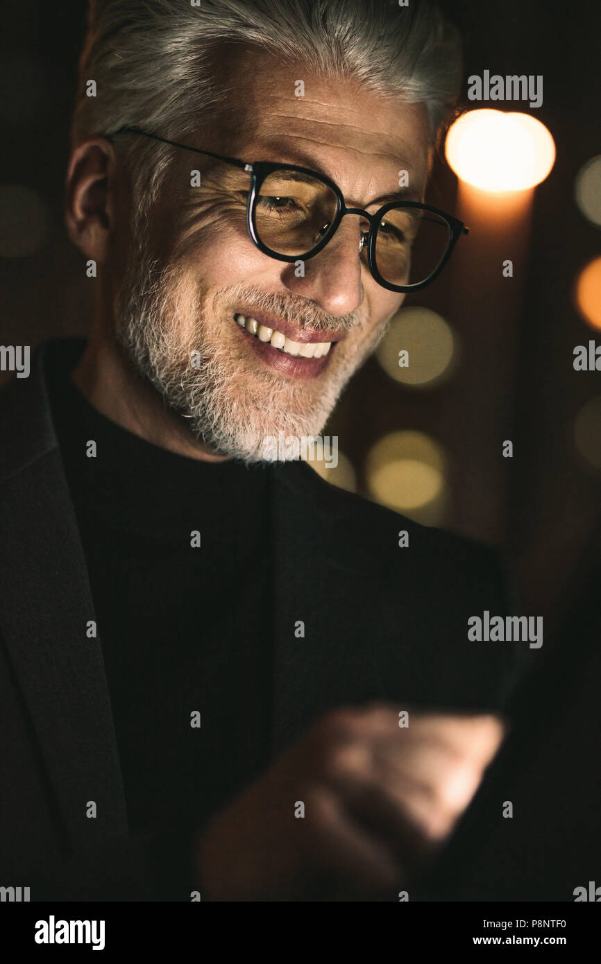 Ravvicinata di un imprenditore sorridente con tavoletta digitale in ufficio. Uomo maturo lavorando in tarda notte in ufficio con tablet pc. Foto Stock