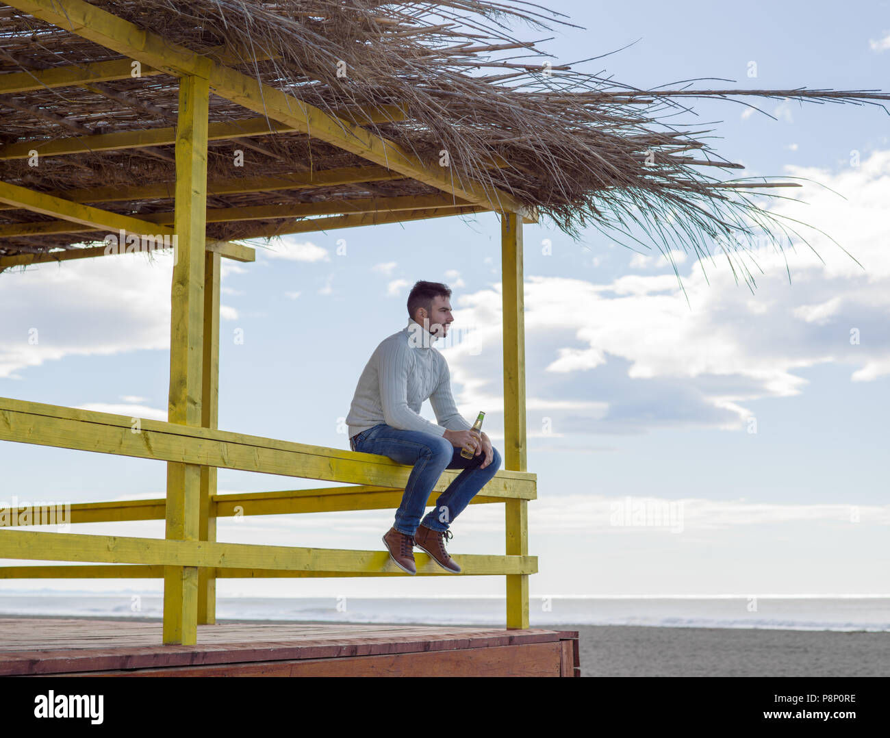 Uomo di bere birra sulla spiaggia durante il periodo autunnale Foto Stock