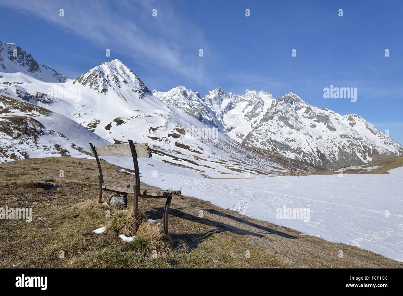 Banco solitario di fronte coperta di neve i prati alpini alla fine dell'inverno al Col de Lautaret Foto Stock