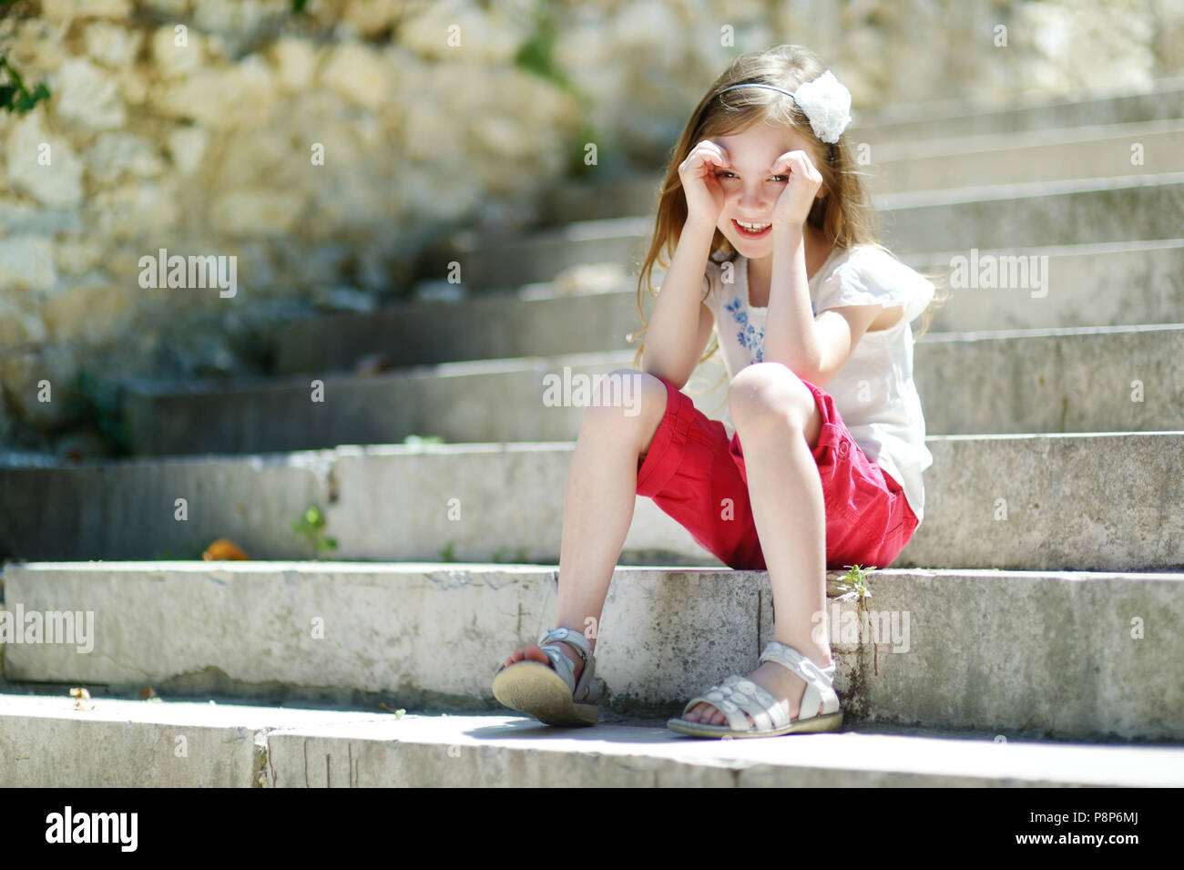 Adorabili poco ragazza seduta sulle scale sul sole e caldo giorno d'estate in tipica città italiana Foto Stock