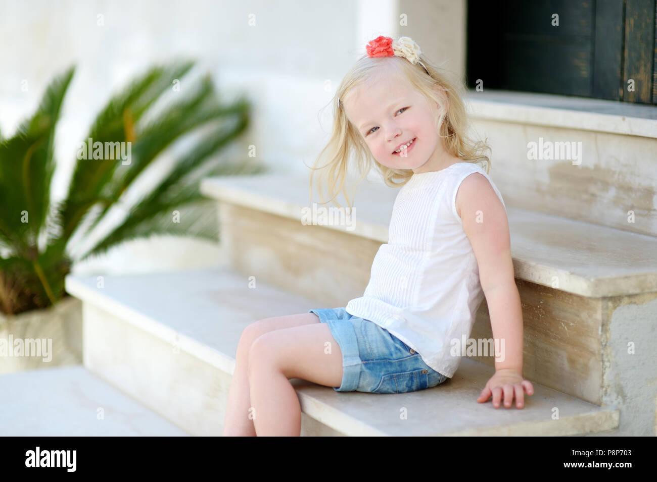 Adorabili poco ragazza seduta sulle scale sul sole e caldo giorno d'estate in tipica città italiana Foto Stock