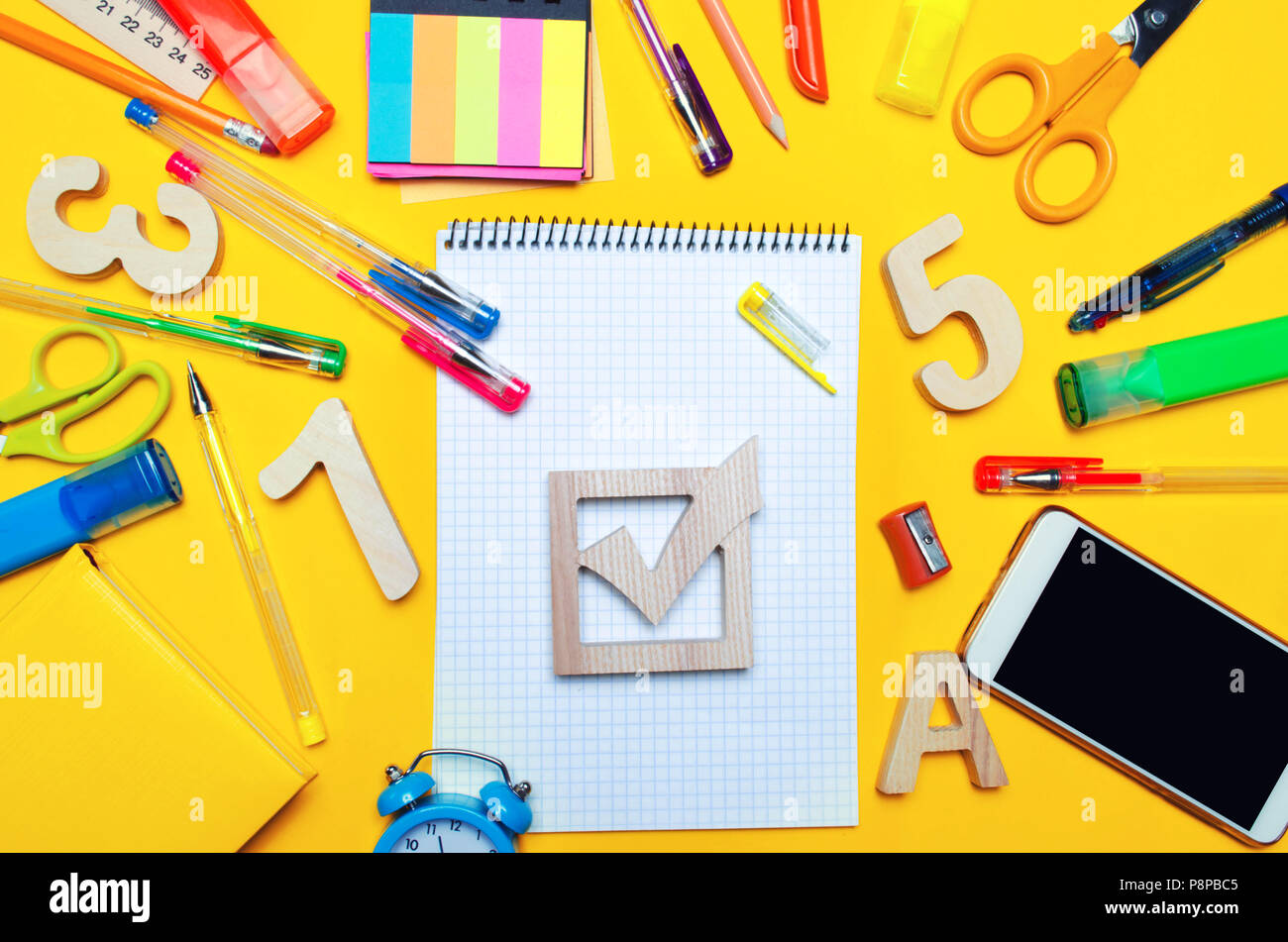 Elezioni scuola concetto. Elezione casella di controllo e la scuola accessori su una scrivania su uno sfondo giallo. L'istruzione. stationery, orologi, penne colorate, ph Foto Stock
