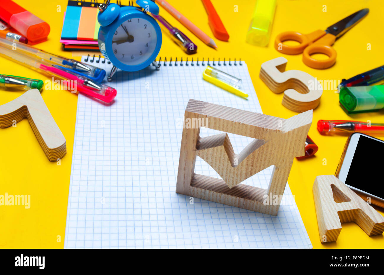 Elezioni scuola concetto. Elezione casella di controllo e la scuola accessori su una scrivania su uno sfondo giallo. L'istruzione. stationery, orologi, penne colorate, ph Foto Stock