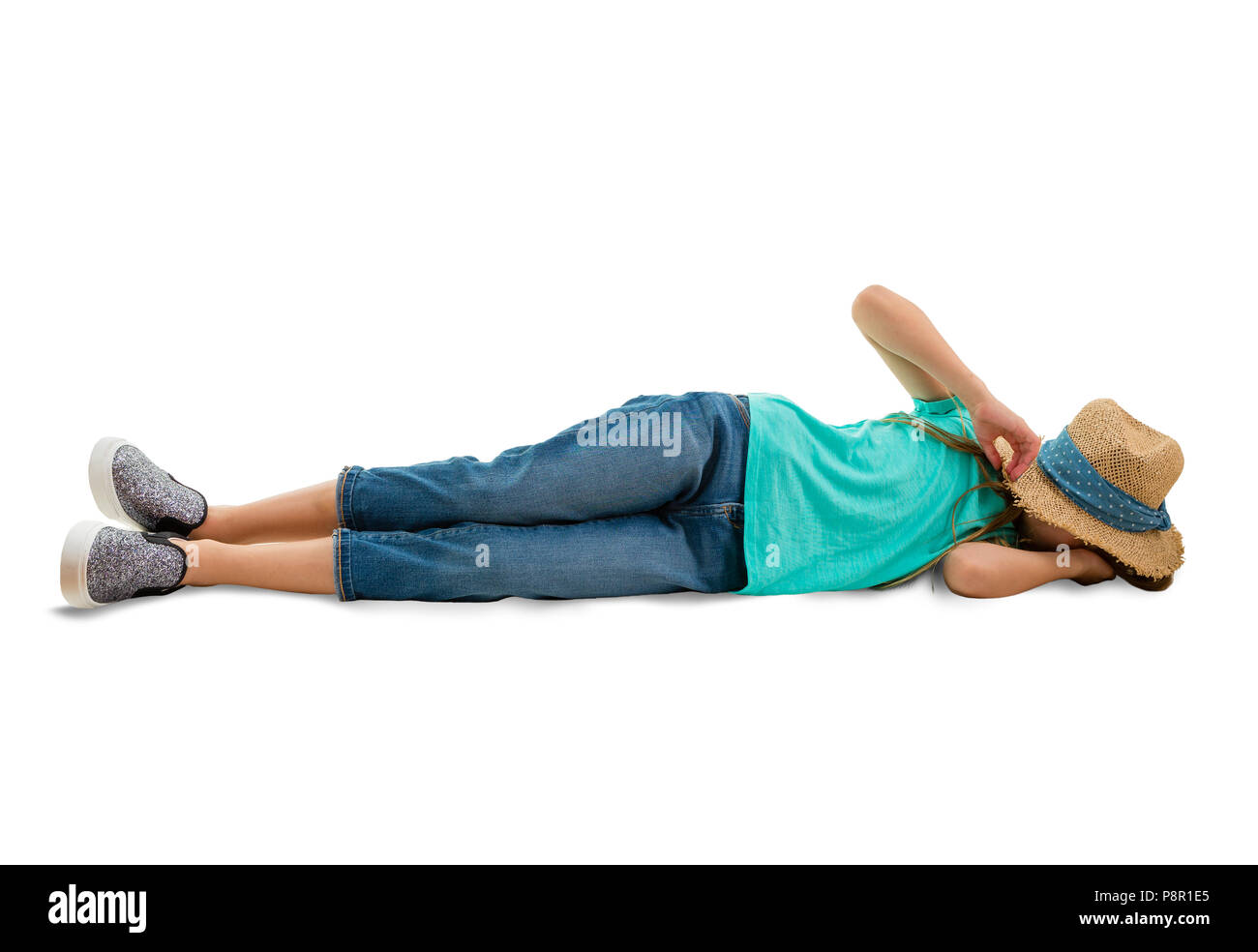 Bambina in jeans e una maglietta blu giacente sul suo lato a terra che copre la faccia con un elegante cappello di paglia isolato su bianco con spazio di copia Foto Stock