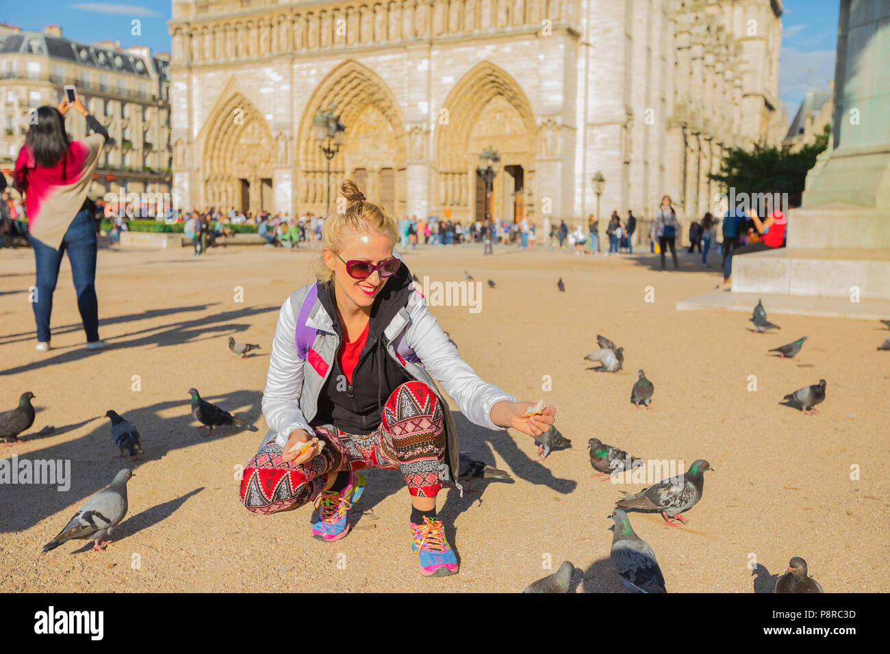 Felice giovane turista donna alimenta i piccioni a Notre Dame square. Stile di vita caucasica traveler gode a Parigi, in Francia, in Europa. Una popolare destinazione turistica nella capitale francese. Foto Stock