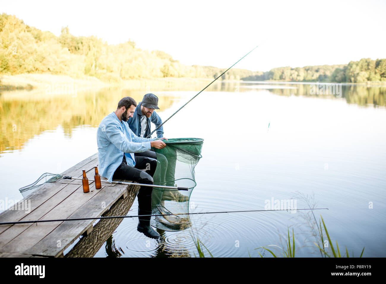 Due felici amici maschi guardando la rete da pesca con pesce durante la pesca sul lago Foto Stock